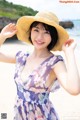 A woman in a dress and hat on the beach.